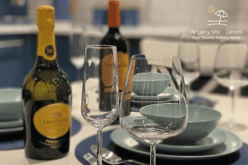 two wine glasses on a table with a bottle of wine at Ar Lan Y Mor - Stunning 2 bed coastal apartment in Llanelli