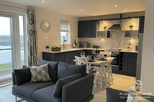 a living room with a couch and a kitchen at Ar Lan Y Mor - Stunning 2 bed coastal apartment in Llanelli