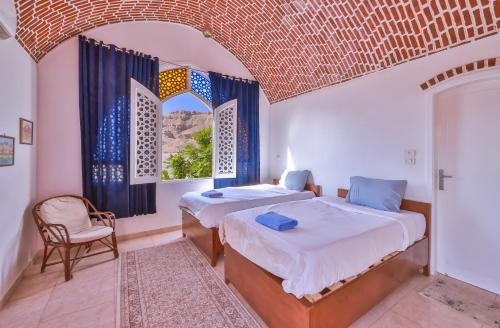 a bedroom with two beds and a chair and a window at Beit El Hanna Valley View in Luxor