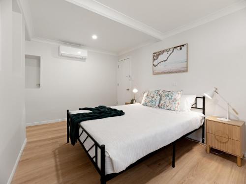 a white bedroom with a bed and a wooden floor at North Ipswich 1BR Pine Studio in Ipswich