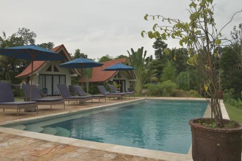 a swimming pool with lounge chairs and umbrellas at Graha Ayoe Resort in Sidemen