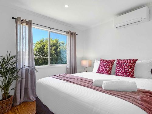 a white bedroom with a large bed with red pillows at The Winegrower's Cottage in Broke