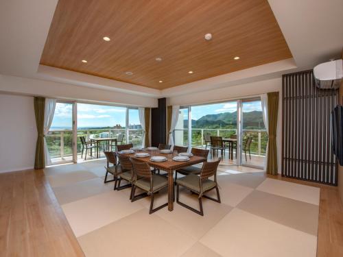 a dining room with a table and chairs and windows at Lieta Nakayama in Nago