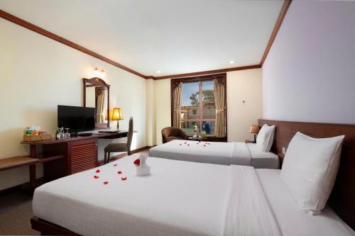 a hotel room with two beds and a desk with a computer at TTC Hotel - Da Lat in Da Lat