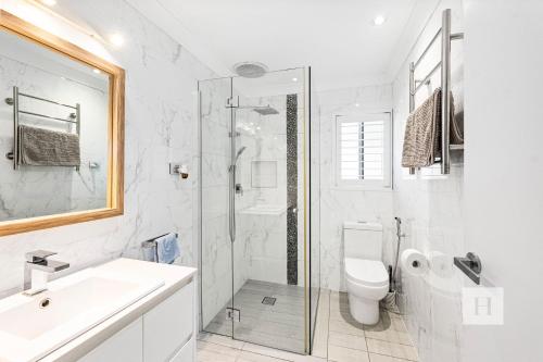 a white bathroom with a shower and a toilet at La Dolce Vita - Your next coastal getaway in Caves Beach