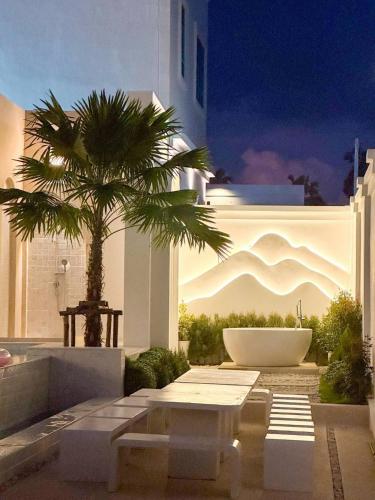 a white building with a palm tree and a bath tub at Brown Empire Pool Villa Pattaya in Nong Prue