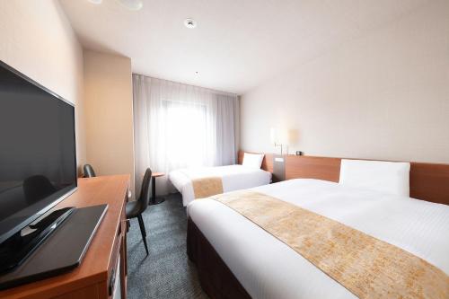 a hotel room with two beds and a flat screen tv at Vessel Inn Yachiyo Katsudai Station in Yachiyo