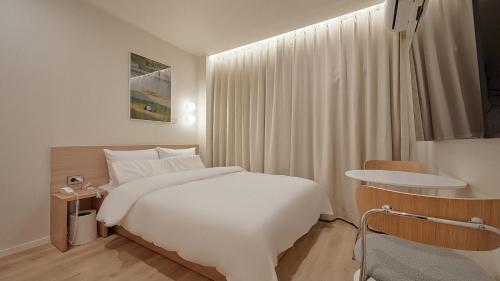 a white bedroom with a bed and a table at Maison de Centum Busan in Busan