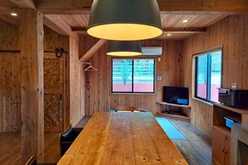 a dining room with a wooden table and a large light fixture at コテージフラミンゴ in Futtsu