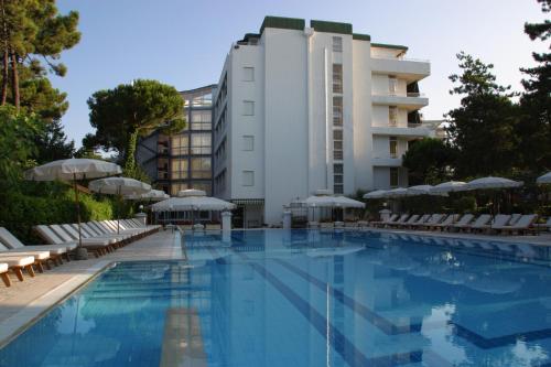 einem Pool mit Stühlen und Sonnenschirmen vor einem Gebäude in der Unterkunft Hotel Greif in Lignano Sabbiadoro