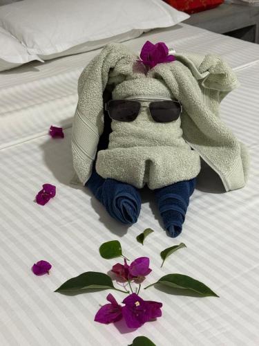 a stuffed animal with sunglasses on a bed with purple flowers at Coconut Villa in Bentota