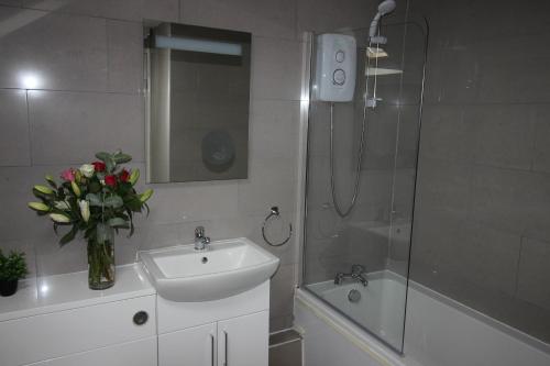 a bathroom with a sink and a shower with a vase of flowers at Cornerhouse Apartments 5 Sleeps 5 in Llandudno