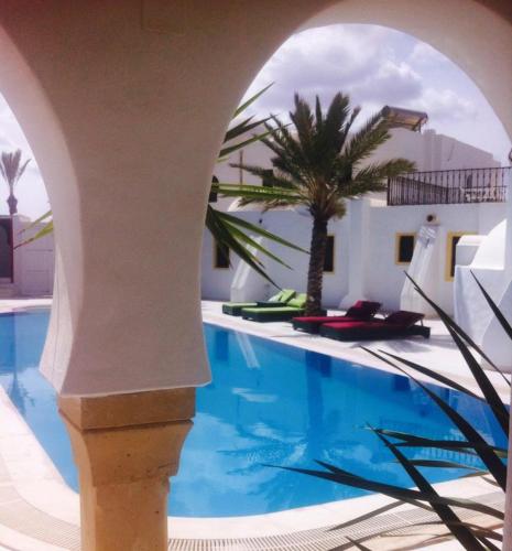 a pool with a palm tree next to a building at Maison Leila chambres d hotes in Midoun