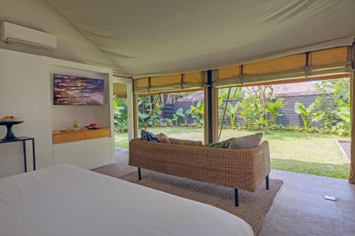 a bedroom with a bed and a couch and windows at Origin Uluwatu in Uluwatu