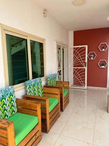 a porch with three wooden chairs and windows at Home away from Home in Komé