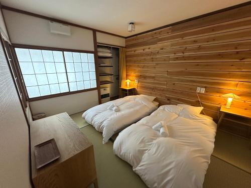 two beds in a room with a wooden wall at My Chalet Hakuba in Hakuba