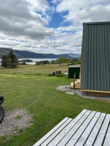 a wooden bench next to a building with a lake at Sterlochy Cabin in Lochcarron