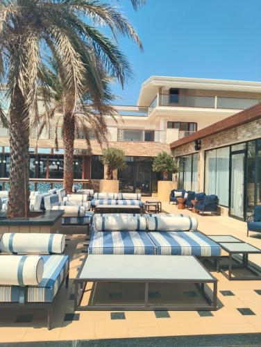 a patio with lounge chairs and palm trees and a building at Peninsula Del Mar Beach Resort in Udupi