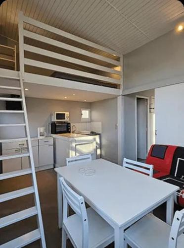 a room with a white table and chairs and a loft bed at Camping des Cèpes in La Salvetat