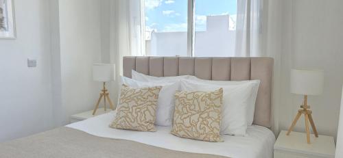 a white bedroom with a bed with pillows and a window at White Aura by Staycom in Paphos