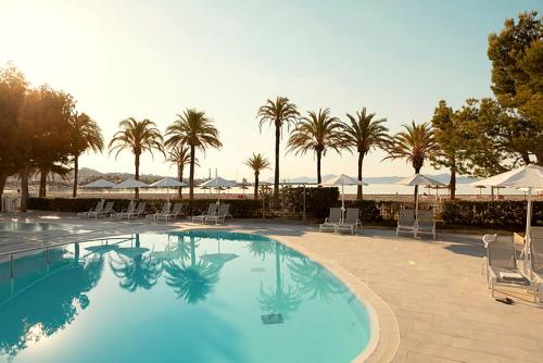 a swimming pool with chairs and umbrellas and palm trees at Sunwing Alcudia Beach in Alcudia