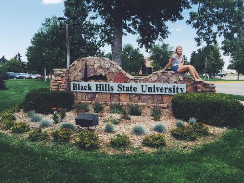 a woman sitting on top of a black hills state university sign at Days Inn by Wyndham Spearfish in Spearfish