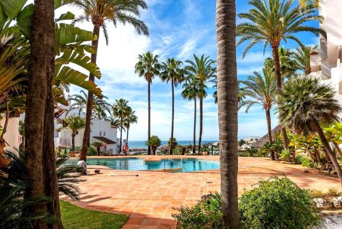 a resort pool with palm trees and the ocean at Fuente de la Duquesa in Manilva