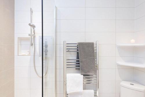 a white bathroom with a shower and a towel rack at Manuka Cottage in Aviemore