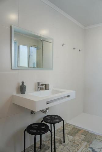 a white bathroom with a sink and two black stools at Canto 30 e UM - HOST & CHILL in Ribeira Grande