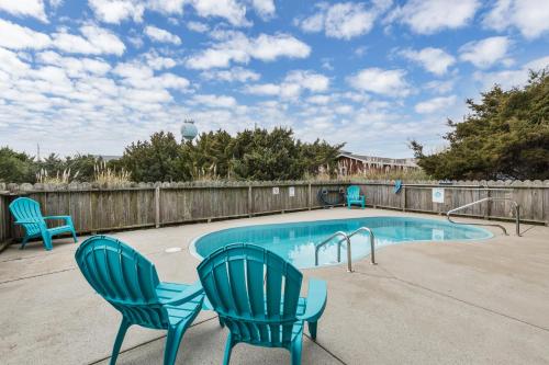 a swimming pool with two blue chairs and a fence at 7030 - Waves Against the Machine in Rodanthe