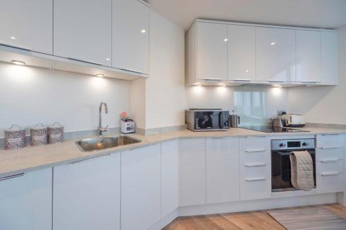 a white kitchen with white cabinets and a sink at Bright 2BR Apartment at Trinity Point in Gravesend