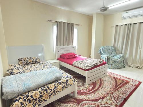 a bedroom with two beds and a chair at Stay home in ‘Uqayr
