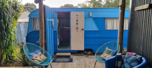 a blue trailer with two chairs in front of it at Raglan West Retro Beach Vibe Accommodation in Raglan