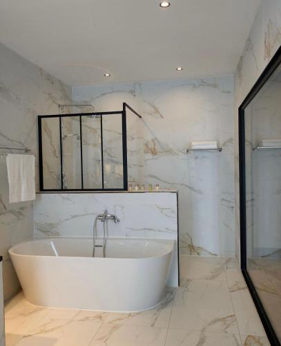 a white bath tub in a bathroom with marble walls at KÓLÒ Hôtel in Yaoundé