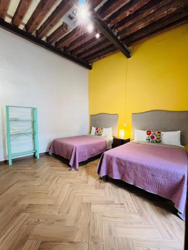 two beds in a room with yellow walls and wooden floors at Casa Universidad in Guanajuato