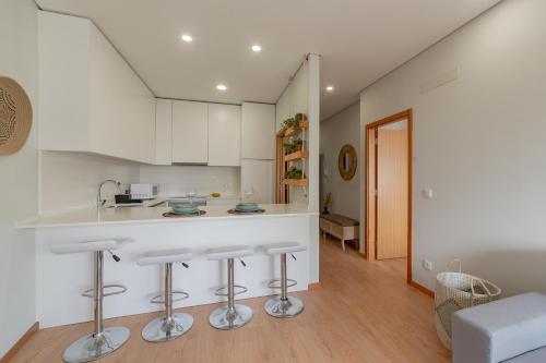 a kitchen with white cabinets and bar stools at 3D Apartamento a 3 minutos da praia in Matosinhos