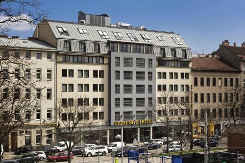 a large white building with cars parked in a parking lot at Flemings Hotel Wien-Stadthalle in Vienna