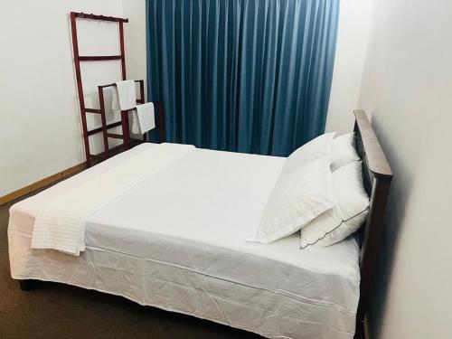 a bedroom with a white bed with a blue curtain at Ceylon Airport Apartment in Raddoluwa