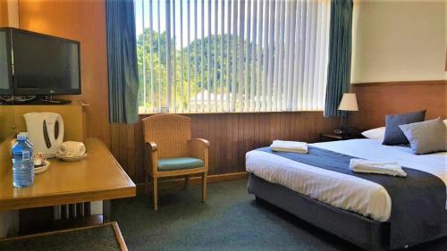 a hotel room with a bed and a desk and a television at Mt Lyell Motor Inn - By Orangepete in Queenstown