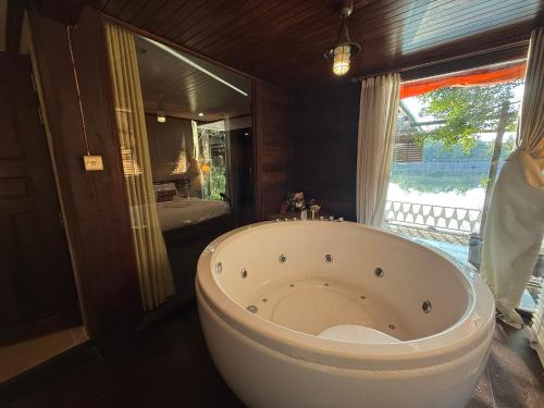 a large white tub in a bathroom with a window at Ban Mali Cafe & Riverside Stay in Ban Chang
