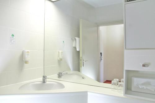 een witte badkamer met een wastafel en een spiegel bij Opal Hotel in Idar-Oberstein