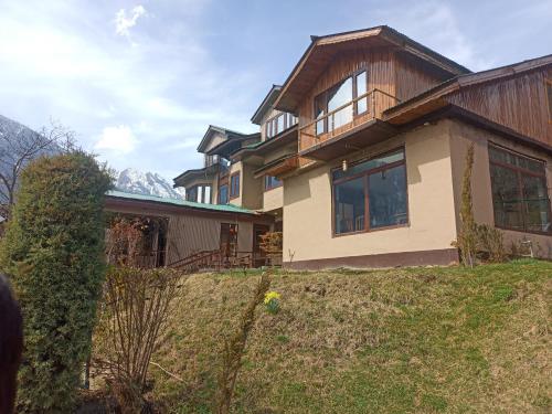 a house on a hill with mountains in the background at Golf view resort in Pahalgām
