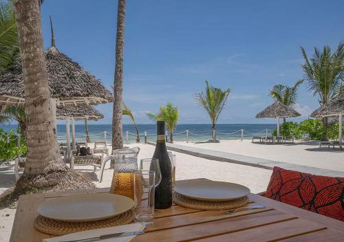 a table with wine bottles and chairs on the beach at Private Beach Front 2-Bedroom Apartment, Groundfloor in Kiwengwa