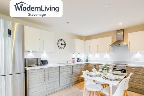 a kitchen with white cabinets and a table with chairs at ModernLiving Stevenage 2 Bedroom Apartment Town Centre Sleeps 8 in Stevenage