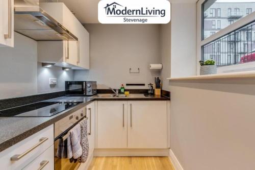 a kitchen with white cabinets and a window at ModernLiving Stevenage 1 Bedroom Apartment Town Centre Sleeps 4 in Stevenage