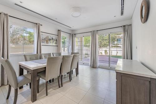 a dining room with a table and chairs and windows at Specious 2BR VILLA WITH MAIDROOM AND HUGE GARDEN IN JVT DUBAI in Dubai