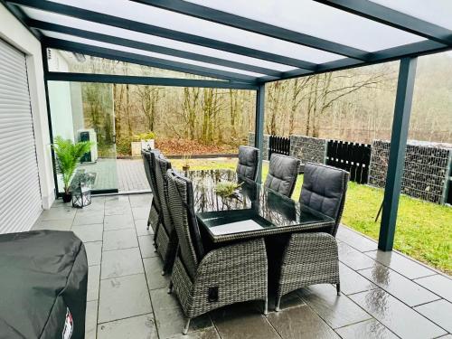 a patio with wicker chairs and a glass table at Ferienhaus Waldblick in Hohenfels-Essingen