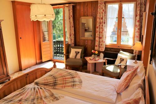 a bedroom with a bed and a chair and windows at Edelweiss Lodge in Wilderswil