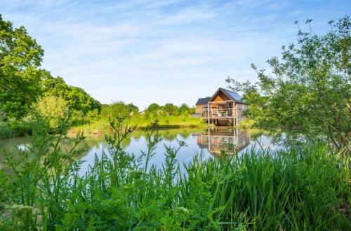 a house on a lake with trees and water at The Boathouse in Biddenden