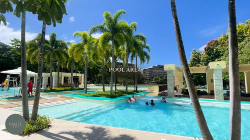 a pool with palm trees and people in it at Nade Suites - Pico De Loro MIB 601 in Nasugbu